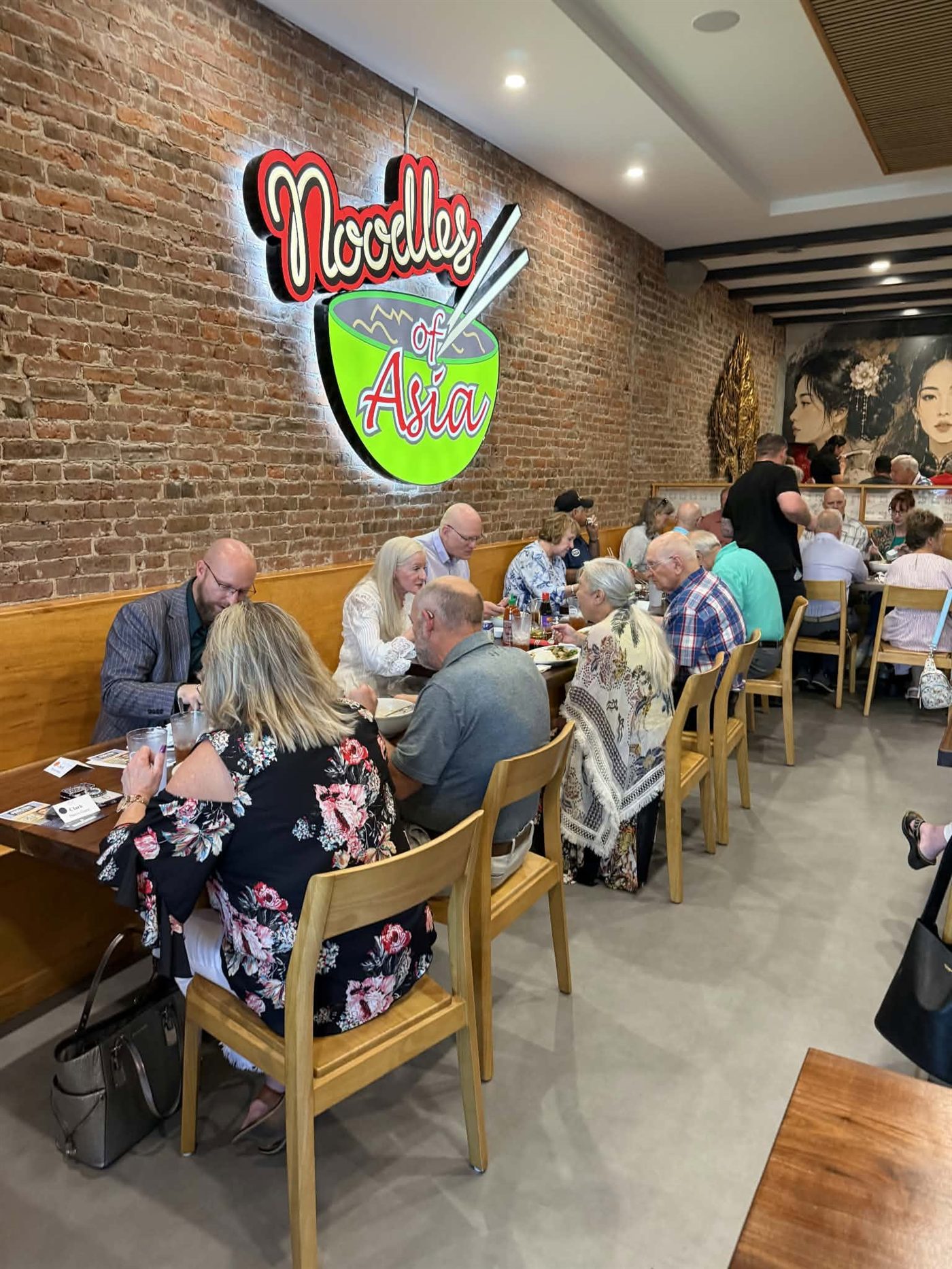 Guests dining beneath the neon Noodles of Asia sign