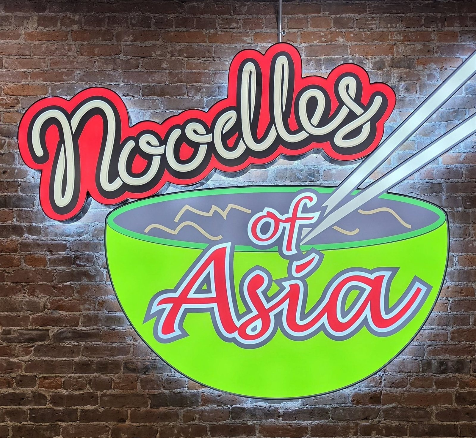 The lit Noodles of Asia sign on the exposed-brick wall inside the restaurant